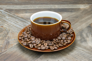 Classic black coffee served in old fashioned brown cup . Fresh coffee beans at the bottom of saucer .