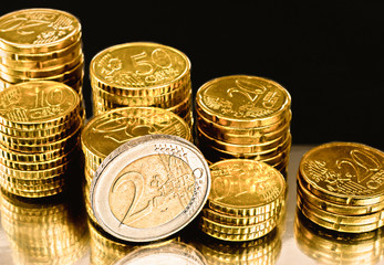 Stacks of European money coins on a shiny surface with black background.