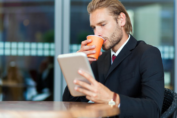 Businessman using his tablet computer while drinking coffee