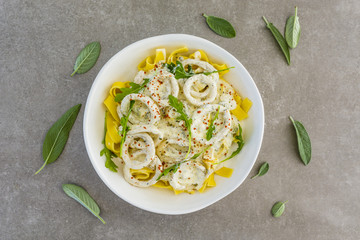 Tagliatele with rings of squid in a creamy sauce on grey background.