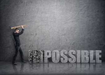 Side view of young businessman crashing 3D concrete 'impossible' words with a hammer