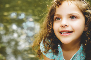 Fototapeta premium Cute little girl wearing beautiful blue dress with matching head band, posing for camera, outdoors lake background