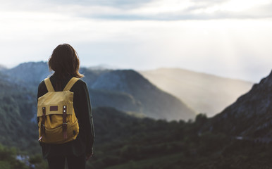 Hipster young girl with backpack enjoying sunset on peak mountain. Tourist traveler on background...