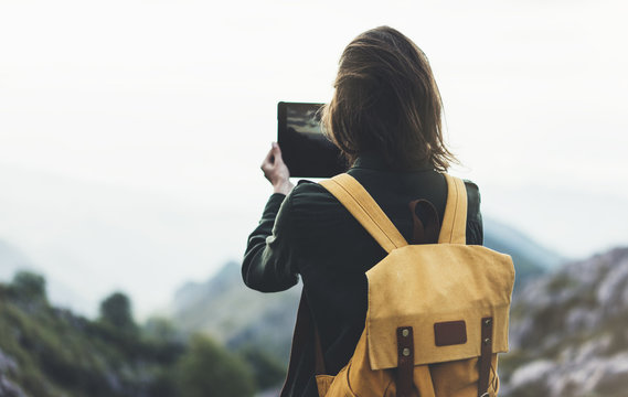 Hipster girl with backpack enjoying sunset on peak of foggy mountain, tourist traveler taking pictures of landscape on mobile sell phone camera on background valley view mockup, hiker photographing