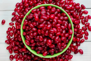 green full plate Cornelian cherries and scattered berry on the white wood board.Selective focus.Top view .A lot of berries