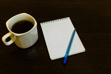 White notepad with a pen on a brown table with a cup of coffee