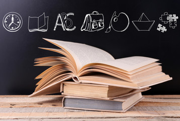Stack of books on wooden table. Icons on blurred blackboard background.