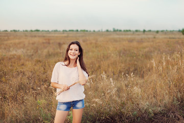 Fototapeta na wymiar Young girl with long brown hair standing at the autumn meadow