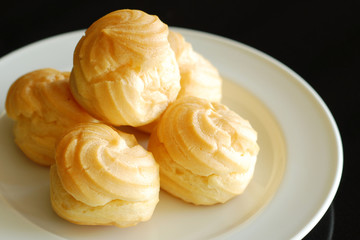 Eclairs or profiterole with chocolate and whipped cream preparing on baking sheet. Spreading chocolate on top of eclair with spoon. Traditional French dessert. Empty space for design text template.