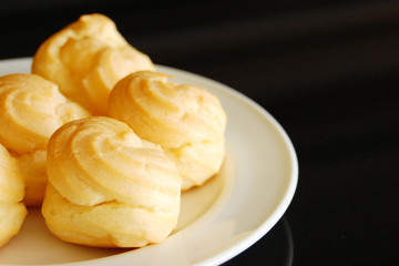 Eclairs or profiterole with chocolate and whipped cream preparing on baking sheet. Spreading chocolate on top of eclair with spoon. Traditional French dessert. Empty space for design text template.