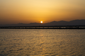 The sun sets behind the mountains behind the lake.