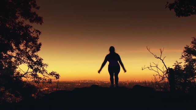 Silhouette of a woman jumping with city in the background. Filmed in slow motion