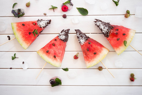 Watermelon slice popsicles on white wooden table with ice and berries Overhead view