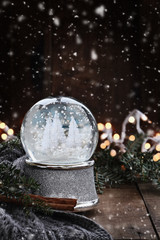 Silver Snow globe surrounded by pine branches, cinnamon sticks and a warm gray scarf with gently...