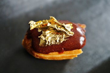 Bite of a chocolate eclair pastry with an edible gold leaf on top