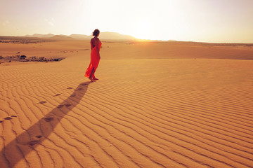 Fototapeta na wymiar Young woman in a long orange dress enjoying the sunset in a dese