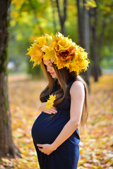 Young pregnant woman in the autumn park with wreath of maple lea