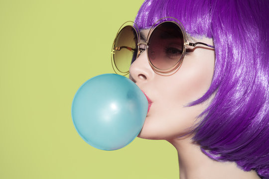 Pop art woman portrait wearing purple wig. Blow a blue bubble ch