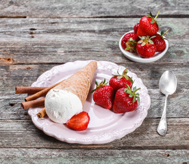 Ice cream with fresh strawberries and jam in waffle cone on plate, on rustic wooden background