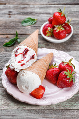Ice cream with fresh strawberries and jam in waffle cone on plate, on rustic wooden background