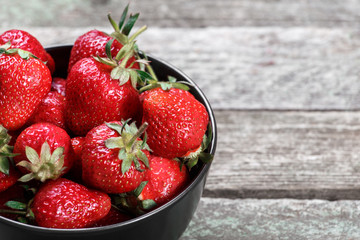 Fresh strawberries in bowl on old wooden background