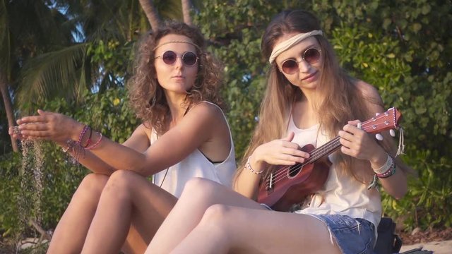 Hippie Girls Having Rest Sitting on a Sand on the Beach at Sunset. Slow Motion
