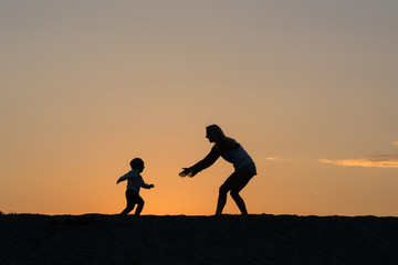 Mother and son playing on the beach at the sunset time.