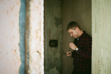 man in a plaid shirt and jeans runs vape juice electronic cigarette. He holds a mechanical mod with RDA. wrists watch and bracelet. against the background of a brick wall