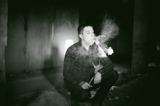 man in a plaid shirt and jeans, smokes an electronic cigarette, blowing smoke and steam from the vaporization a mechanical device. fashionable hobby, alternative to smoking cigarettes, glycerin clouds