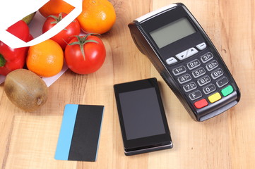 Payment terminal, mobile phone with NFC technology and credit card, fruits and vegetables, cashless paying for shopping