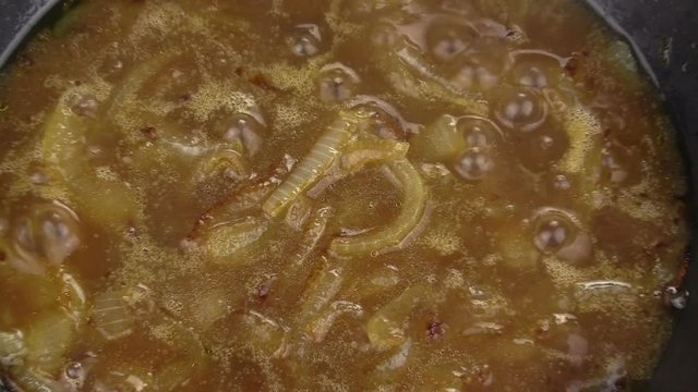 Zoom back from close up of caramelized onions frying in a pan.
