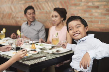 Cheerful little boy sitting at table during family dinner