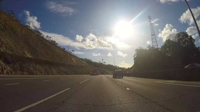 4K Vehicle POV, driving along the freeway through tunnels from Adelaide Hills to Adelaide City, South Australia, time-lapse with afternoon sun and lens flare.