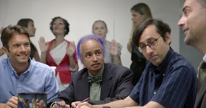 Business men high five each other in meeting while excluded female colleagues stand outside glass walls of conference room.  Medium shot, low angle, recorded hand held in real time.