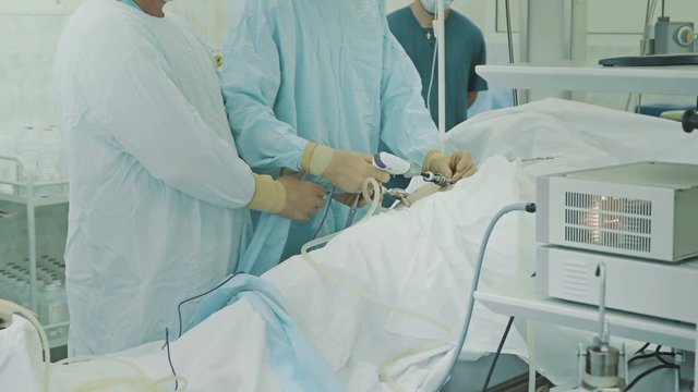 Laparoscopic Surgeons team performing real operation in operating room. Surgeon operating patient, knee replacement nurse adding tools surgeon, surgical instruments, holding hands
