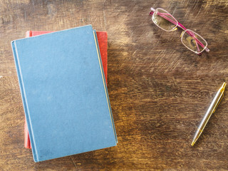top view of book, pen and glasses on wooden background