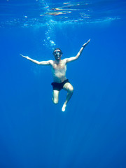 Obraz premium Portrait of a young causasian man meditating in the lotus position underwater. Submerged under water free diving, crossed legs, wearing a mask and blowing bubbles.