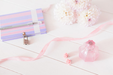 Chrysanthemum, perfume, earrings, ribbon, notebook and pen on white background. Casual creative lady home office.