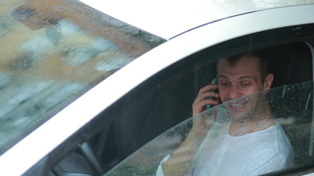 man talking on a cell phone while sitting in the car. smiling driver