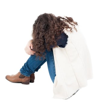 back view curly girl sitting and crying. girl relaxes. Rear view people collection. backside view of person. Isolated over white background.  A girl in a white tank top sitting on the floor with his