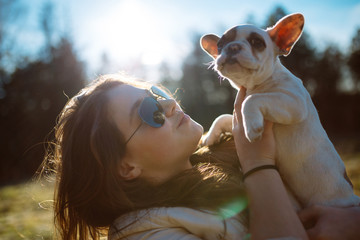 Cute teenager girl enjoying outdoors with her beautiful French bulldog puppy. Sunny autumn day. Short depth of field and strong back light and flare.
