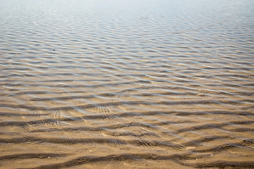 Gentle waves on the shallow water; water surface for background shallow of sea on sand along beach side.