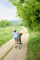 Relaxing in the nature. Rear view shot of a young woman pushing her bike at rural scene. 