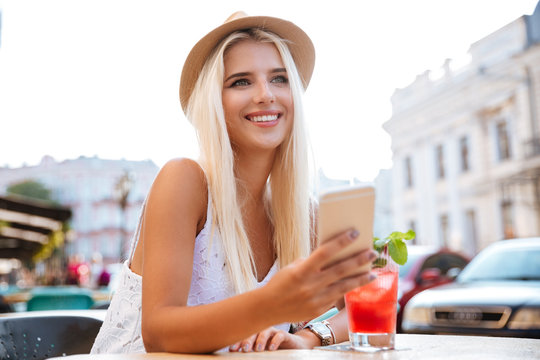 Woman in hat using smartphone while sitting at cafe outdoors