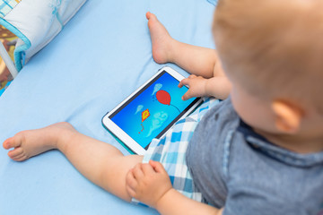 Baby boy sitting with digital tablet in bed