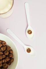 Top view of chocolate cereal serving in spoons with milk on purple background.
