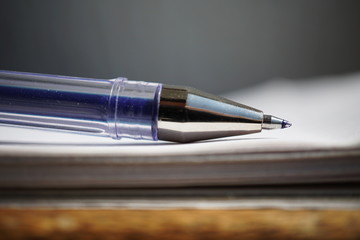 Detail of a sharp tip of the blue ball pen on the white lined notepad as a symbol of business office stationary 