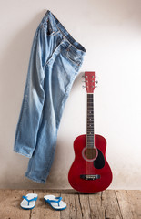 still life photography : old guitar with jeans hang on the wall and old rubber slippers on old wood in rustic concept