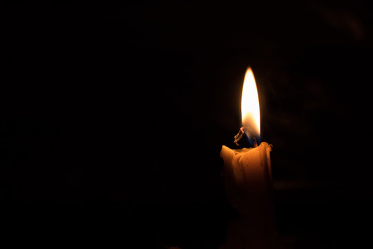 One light candle burning brightly, image is isolated against a b