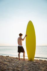 Man with his surfboard standing on the beach